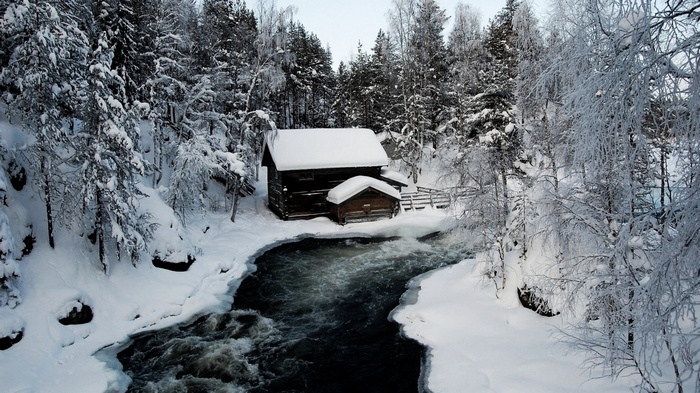 Wooden cabin by a river in a snowy forest