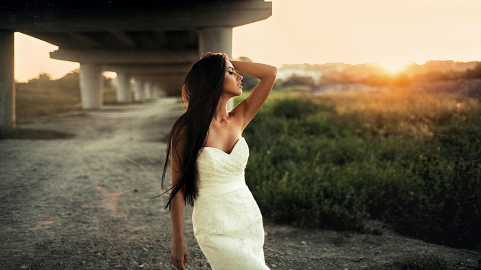 Woman in white dress under bridge at sunset