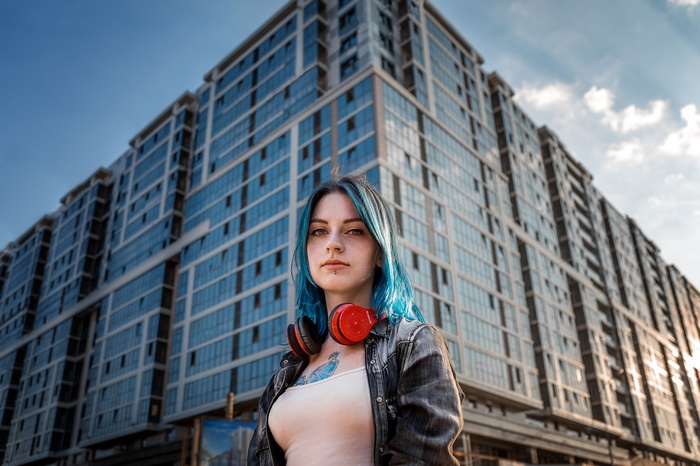 Woman with blue hair and headphones in front of a building
