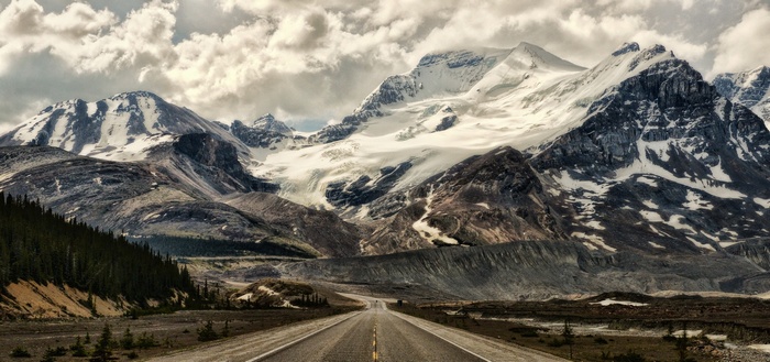 Road leading to snow-capped mountains under cloudy sky