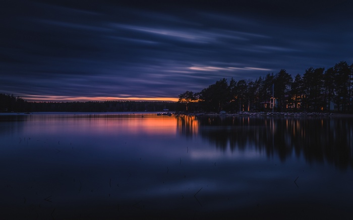 Sunset over a lake with trees and a house in Finland
