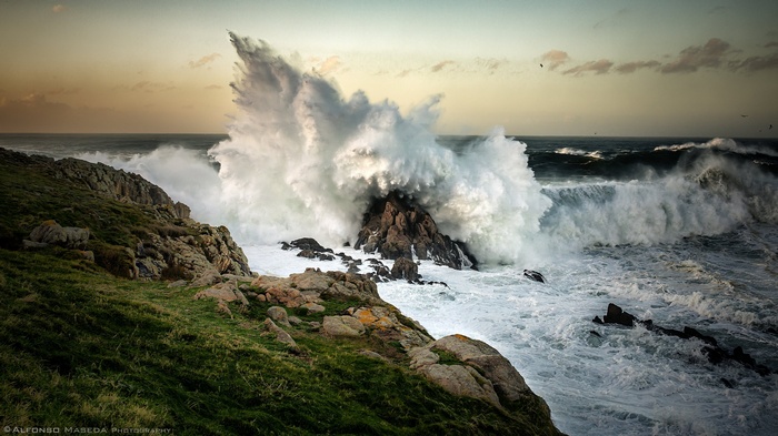 Massive waves crash against rocky shore at sunset
