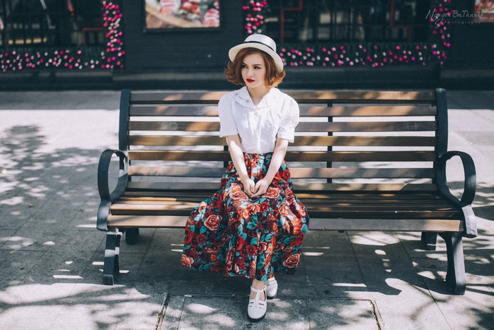 Woman in floral skirt and hat sitting on a bench