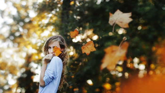Woman with leaf covering eye in autumn forest