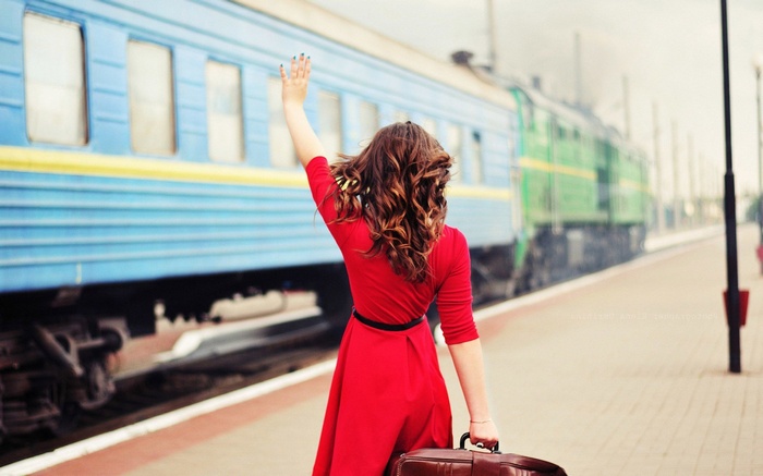 Woman in red dress waving goodbye at train station
