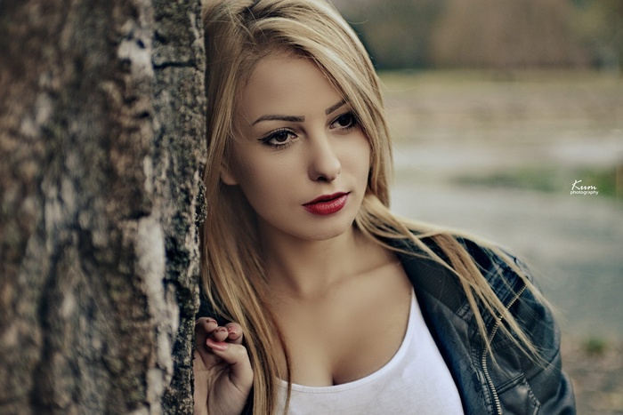 Blonde woman with red lipstick leaning on a tree