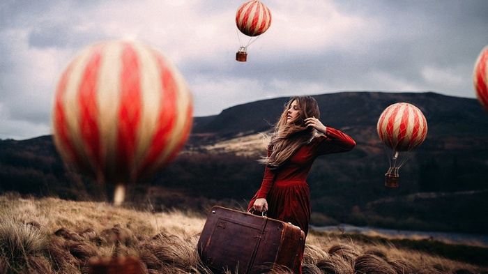 Woman with suitcase and hot air balloons in a field