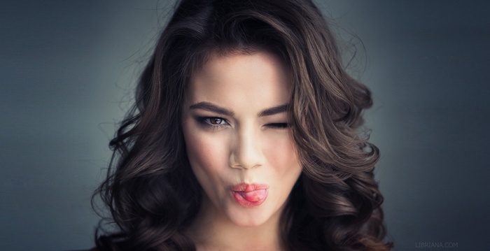 Woman with long wavy brown hair winking and sticking out her tongue