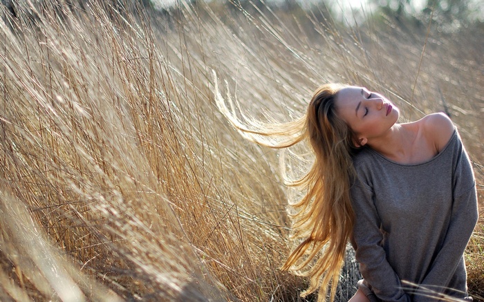Woman with long blonde hair in a field of dry grass