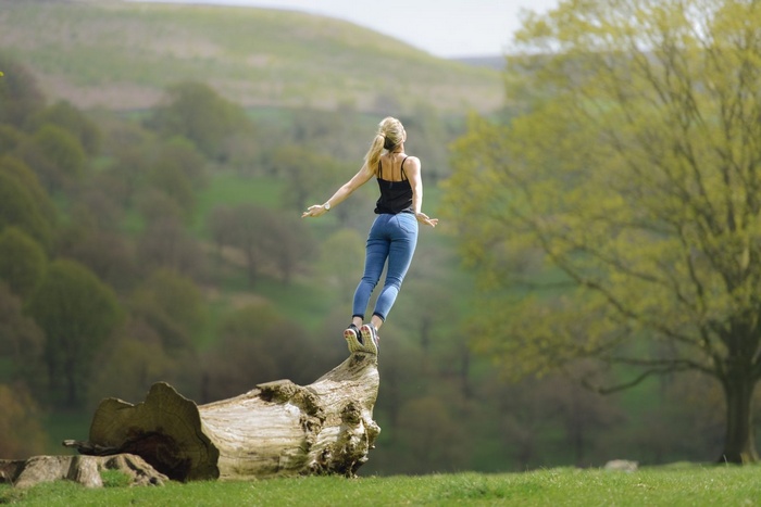Woman jumping on a log in a grassy field