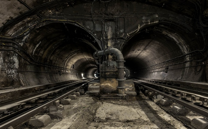 Abandoned subway tunnel with tracks and pipes