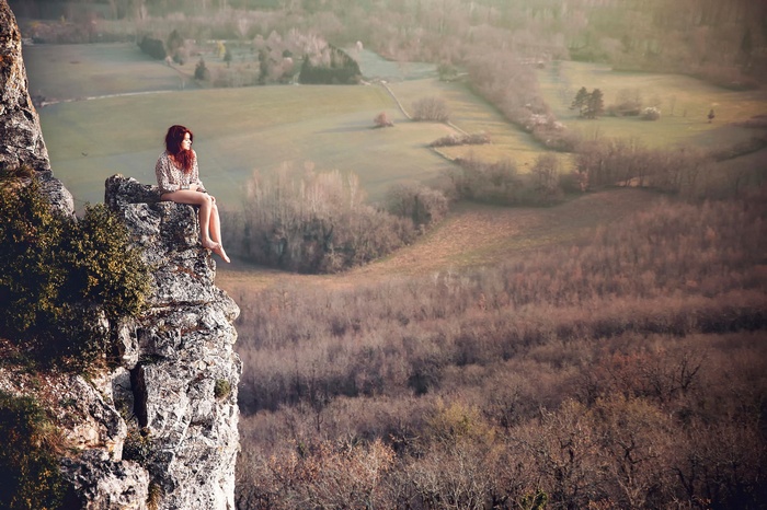 Woman sitting on a rocky cliff overlooking a valley