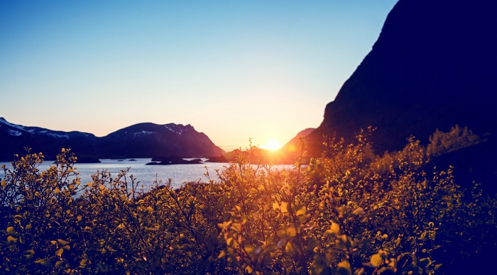Sunset over a calm body of water with mountains and bushes