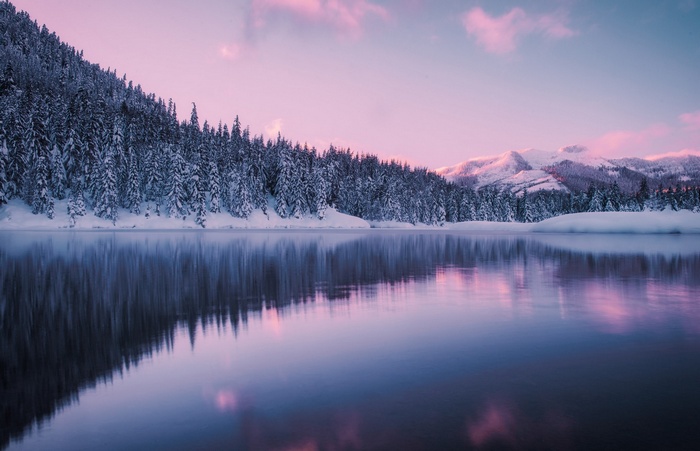 Snowy forest and mountains reflected in a lake at sunset
