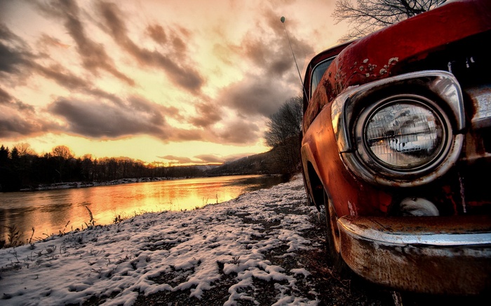 Old red truck by a river at sunset
