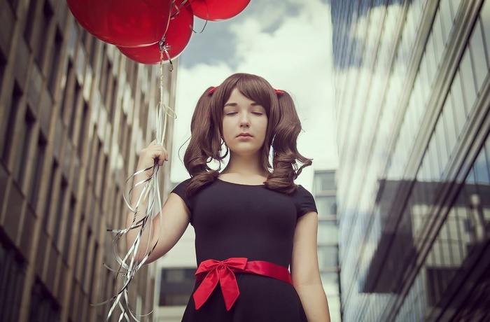 Woman in black dress with red bow holding red balloons