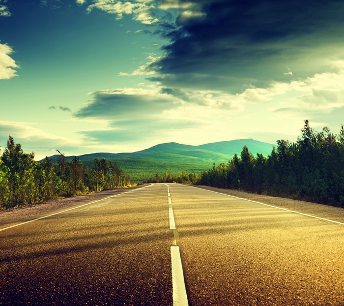 Open road through a green landscape with mountains