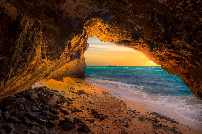 Cave opening to a beach and ocean at sunset