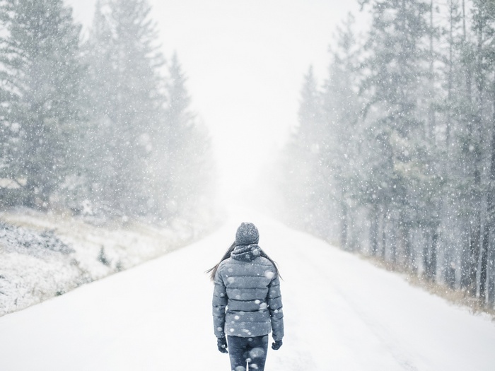 Woman walking on a snowy road surrounded by trees