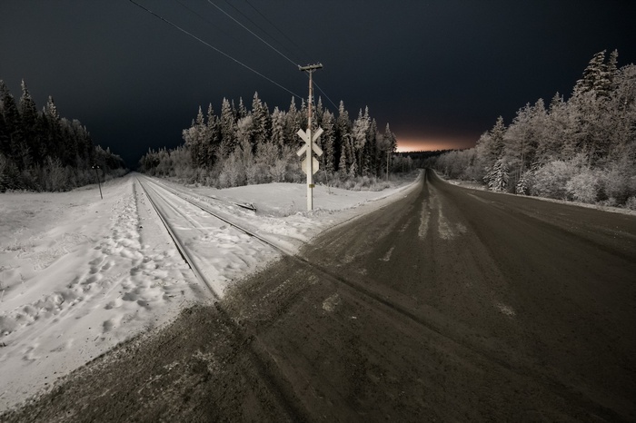 Snowy railway crossing at night with a road