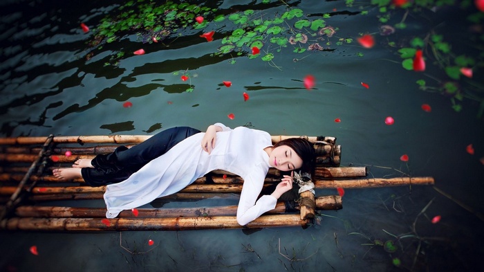 Asian woman in white dress lying on bamboo raft