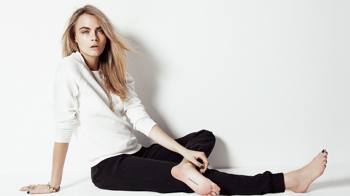 Cara Delevingne sitting barefoot on white background