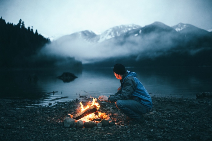 Man by campfire near lake and mountains