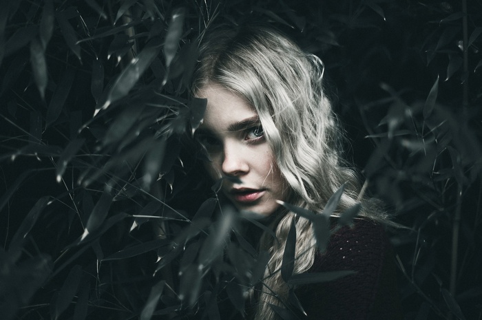 Woman with blonde hair peeking through plants