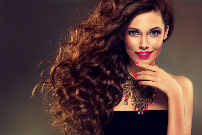Woman with long curly brown hair and bright makeup