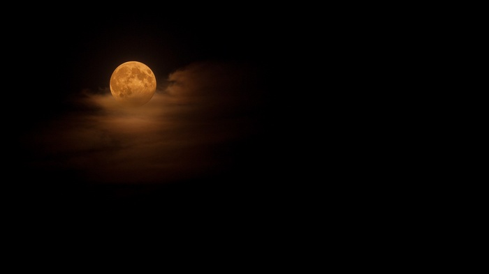 Orange moon peeking through dark clouds