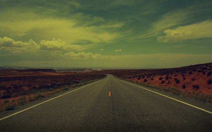 Desert road stretching into the distance under a cloudy sky