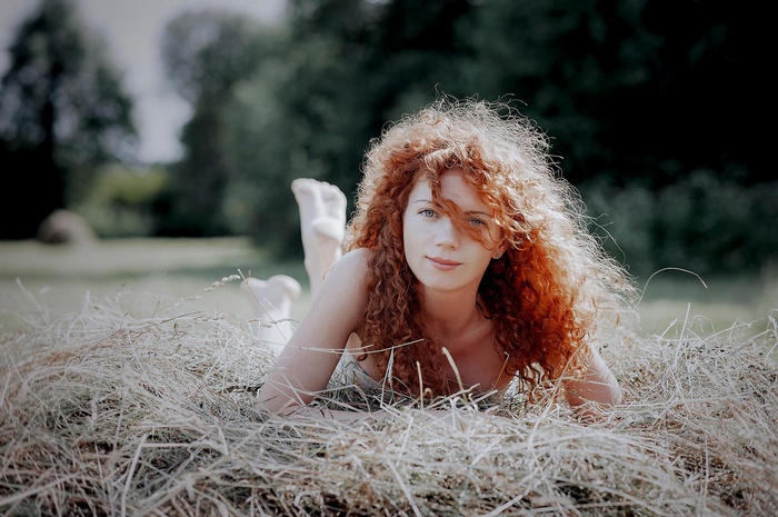 Redhead woman with curly hair lying in straw