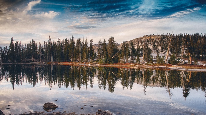 Lake reflection of trees and mountains under cloudy sky