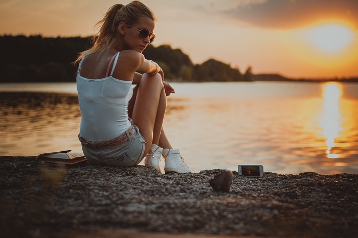 Woman in jean shorts sitting by the river at sunset