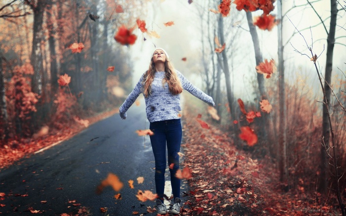 Woman in sweater and jeans in autumn leaves