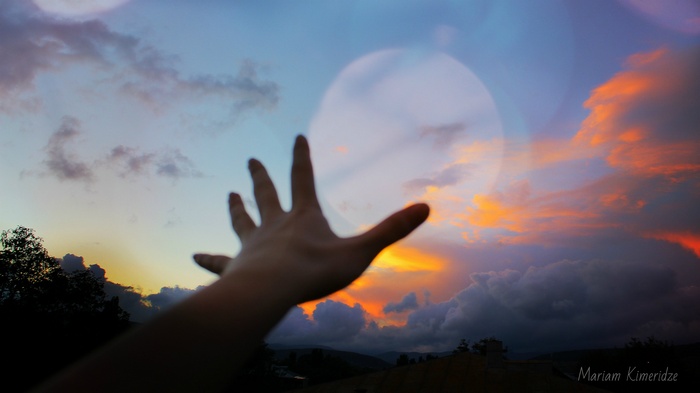 Hand reaching towards a colorful sunset sky