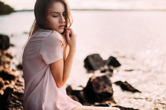 Woman sitting by the water at sunset