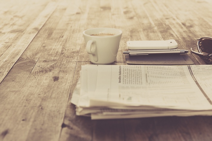 Coffee cup, smartphone, pen, and newspaper on a wooden table