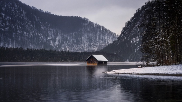 Wooden boathouse on a lake with snow-covered mountains