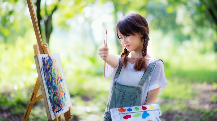 Asian woman painting outdoors with easel and palette