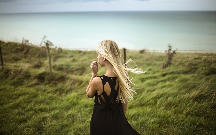 Woman in black dress on a grassy field overlooking the sea