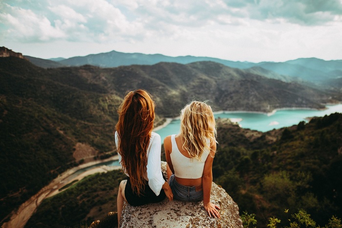 Two women sitting on a rock overlooking a mountain landscape