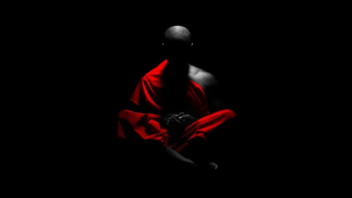Monk meditating in red robes on black background
