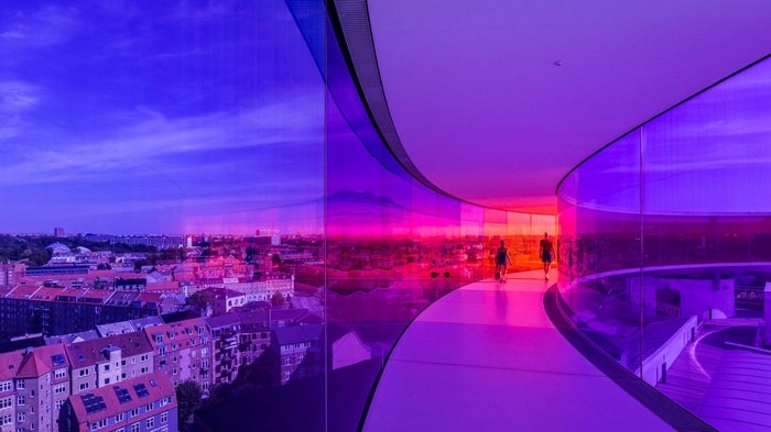 People walking in a colorful glass hallway overlooking Aarhus, Denmark