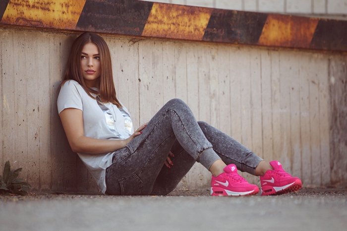 Woman in jeans and pink sneakers sitting by a wall