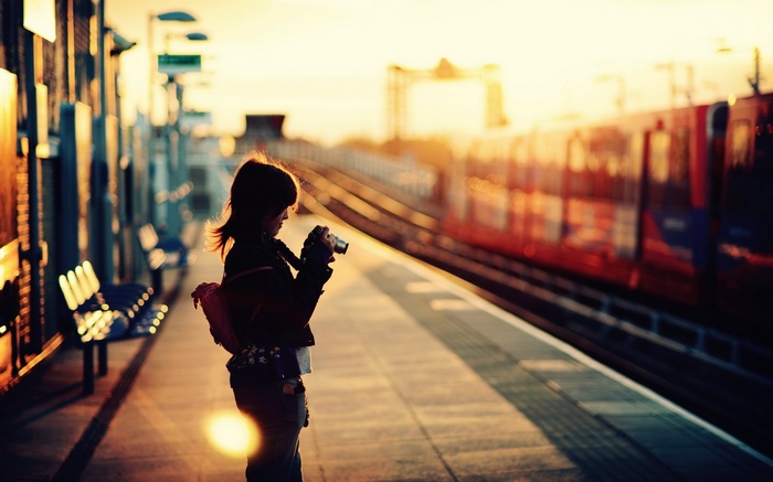 Girl with camera at a train station during sunset
