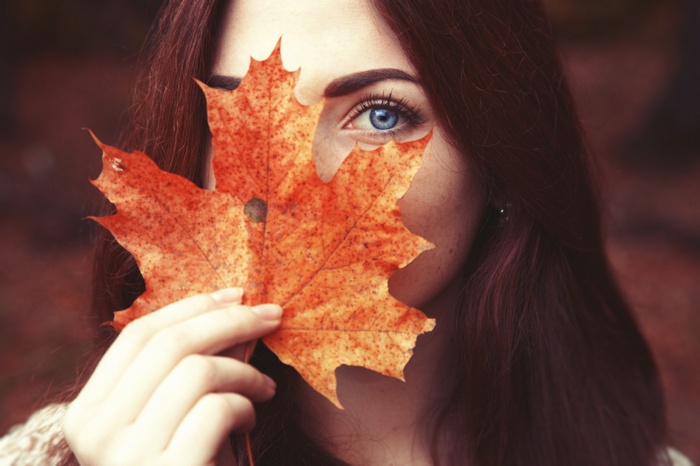 Woman with blue eyes holding an autumn leaf