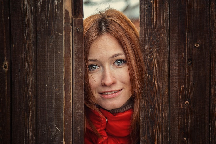 Woman with red hair peeking through wooden fence