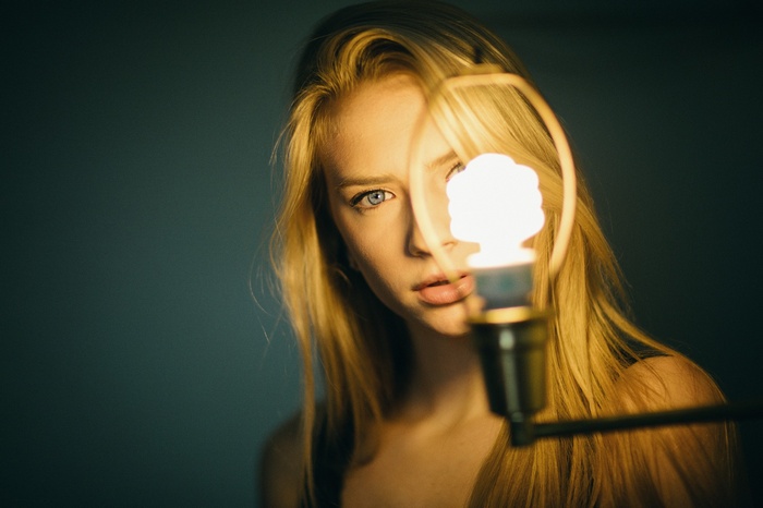 Woman with blonde hair and blue eyes in front of a lightbulb