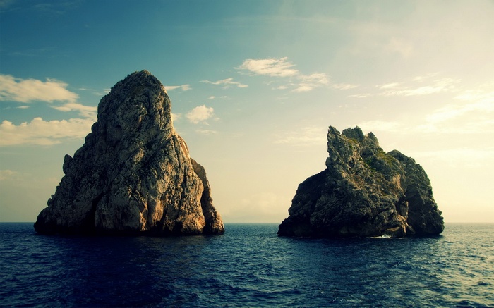 Two large rock formations in the sea under a cloudy sky